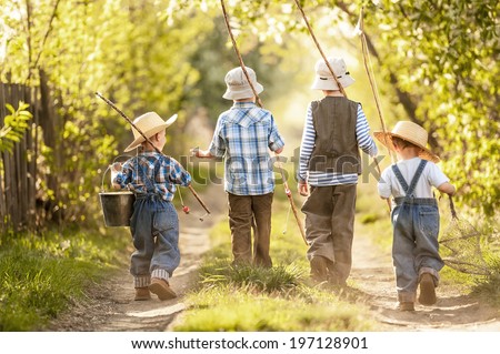 Four boys with fishing rods go on a fishing trip on the narrow rural road in sunny summer day