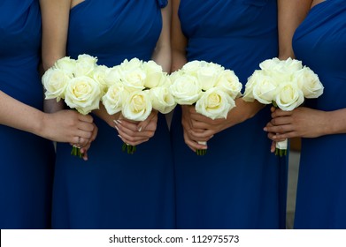 four bridesmaids in blue dresses holding white rose bouquets