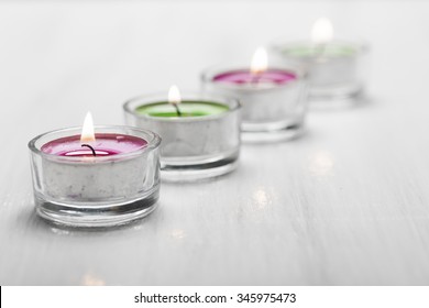 Four Burning Tea Lights on a white wooden surface. 