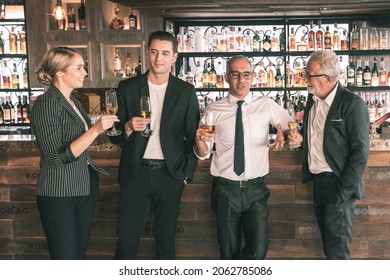 Four Business Partner Celebrating Their Victory. Old Business Man Making A Toss To Younger Business Man And Woman. They Are Holding A Champagne Glass In A Hotel Lobby With City Scape Background.