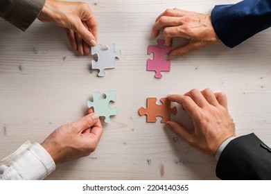 Four business people holding matching puzzle pieces of various pastel colours in a conceptual image of business teamwork and cooperation. - Shutterstock ID 2204140365