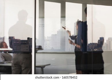 Four Business People Standing And Looking At  White Board On The Other Side Of Glass Wall