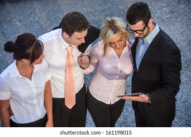 Four Business People Standing On Street Looking At A Tablet
