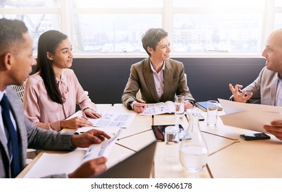 Four Business Professionals Conducting A Meeting In A Bright Modern Conference Room With A Large Windown And An Abundance Of Natural Light, While Making Use Of Technology To Optimise Efficiency.