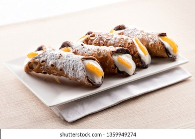 Four cannoli Sicilia, or Sicilian cannoli, deep fried pastry tubes with a sweet ricotta filling garnished with colorful orange rind and served on a rectangular plate