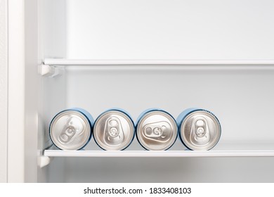 Four Cans Of Beer Or Soda On The Shelf In An Empty Home Fridge. Cooling Beverages In Aluminum Cans With Pull Tabs Before Drinking. Copy Space. Front View.