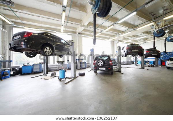 Four cars on lifts and on floor\
in small service station. Cars prepared to diagnosis and\
repair.