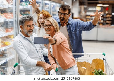 Four cheerful customers are taking a selfie with a smartphone while having fun shopping together in a supermarket, making funny faces and gestures - Powered by Shutterstock