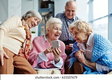 Four cheerful elderly people hanging out in spacious coffeehouse and looking through photos on modern smartphone - Powered by Shutterstock
