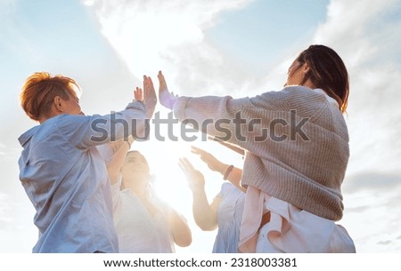  Four cheerful laughing women rising hands Up making High Five during outdoor walking with bright evening sun backlight. Woman's friendship, natural diversre beauty, relations, happiness image