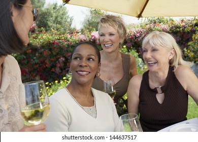 Four Cheerful Multiethnic Middle Aged Women Chatting With Wine Glasses At The Garden Party