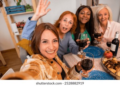 Four cheerful multi-generational women are posing for a selfie while having christmas dinner at home. One of them is waving her hand - Powered by Shutterstock