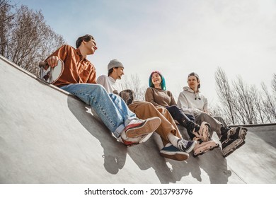 Four cheerful teenagers are happy to meet at the city skatepark, joke and share their impressions after roller skating and skateboarding