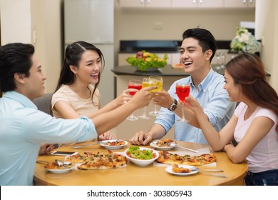 Four cheerful young friends clinking glasses at the dinner