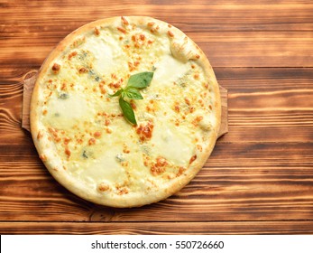 Four cheese pizza quattro fromaggi with basil leaf on a rustic wooden board background