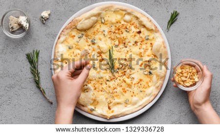 Four cheese pizza. Woman decorating pizza with chopped nuts, top view