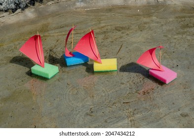 Four Children's Colorful Ships Are Floating In A Shallow Pond. The Toy Sailboats Are Made From Kitchen Sponges. Summer, Daytime. Selective Focus. No People.