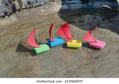 Four Children's Colorful Ships Are Floating In A Shallow Pond. The Toy Sailboats Are Made From Kitchen Sponges. Summer, Daytime. Selective Focus. No People.