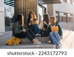 Four college friends sitting on sunlight in front of a college building