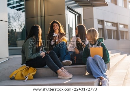 Four college friends sitting on sunlight in front of a college building