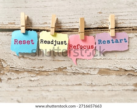 Four colorful speech bubble notes showing motivational words—reset, readjust, refocus, restart—clipped on a string for encouragement and personal growth.
