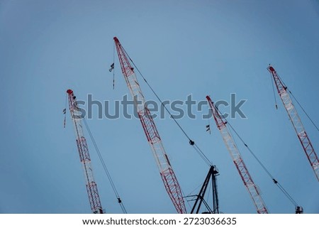 four construction cranes, red and white, against a clear blue sky, horizontal