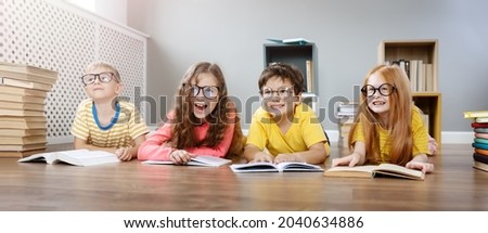 Four cute children in glasses lying on the floor indoors with books. Concept of hobby and education.