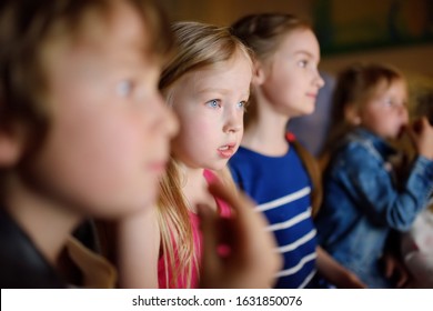 Four Cute Kids Watching A Movie At Home. Children Having Fun In Front Of The TV. Kids Playing Video Games In Dark Room At Home.