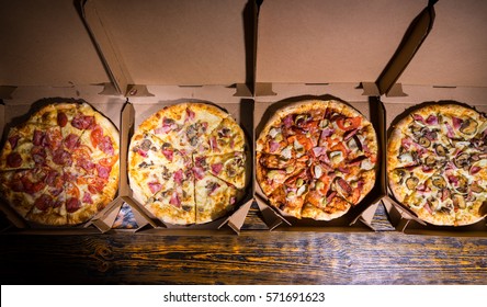 Four different delicious pizzas in boxes on wooden table