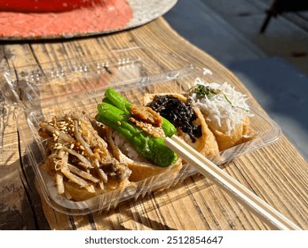 Four different pieces of Inari sushi in a takeout plastic container, along with wooden chopsticks - Powered by Shutterstock