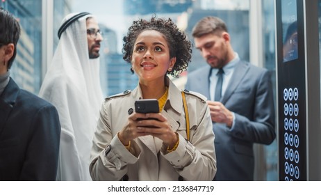 Four Diverse Multiethnic International People Ride a Glass Elevator to Office in a Modern Business Center. Focus on Young Stylish Black Latin Businesswoman Using Smartphone in a Lift. - Powered by Shutterstock