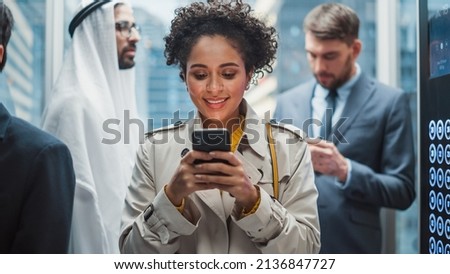 Four Diverse Multiethnic International People Ride a Glass Elevator to Office in a Modern Business Center. Focus on Young Stylish Black Latin Businesswoman Using Smartphone in a Lift.