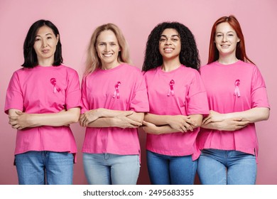 Four diverse women of different ages and ethnicities are standing together, wearing pink t-shirts with pink ribbons, symbolizing their support for breast cancer awareness month - Powered by Shutterstock