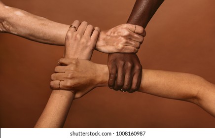 Four diverse women holding each others wrists in a circle. Top view of female hands linked in the lock against brown background.