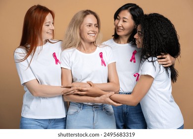 Four diverse women are smiling and showing their support for a friend battling breast cancer standing isolated on beige background. Support, health care concept - Powered by Shutterstock