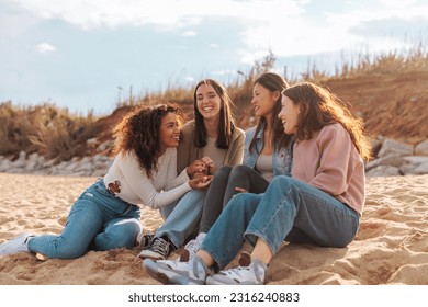 Four diverse young women gossiping while sitting on the beach - Powered by Shutterstock