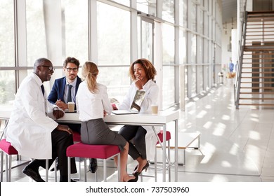 Four Doctors Talking At A Table In A Modern Hospital Lobby