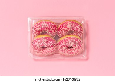 four donuts in a pink glaze with a white sprinkles on a pink background. Sweets and desserts. Copy space. Symbol for environmental pollution done by the food industry