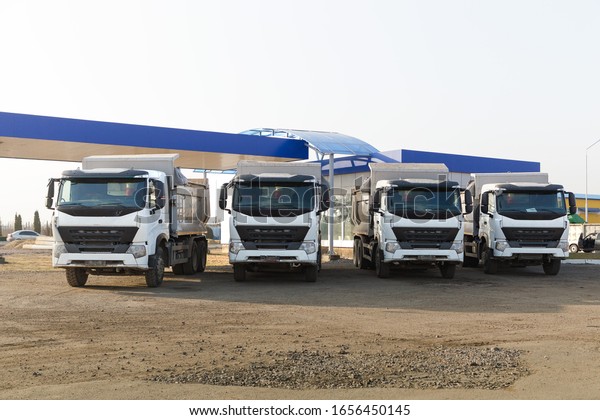 \
Four dump trucks with clean white cabs stand\
beautifully next to each other on a dirt road backlit by the sun.\
Delivery, construction. Copy\
space