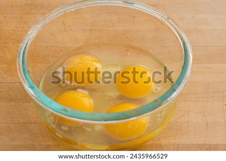 Four eggs in a glass bowl on cutting board.  