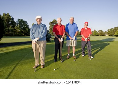 Four elderly men are standing together on a golf course. They are holding their clubs, smiling, and looking at the camera.  Horizontally framed shot.