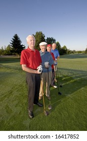 Four elderly men are standing together on a golf course. They are holding their clubs, smiling, and looking at the camera.  Vertically framed shot.