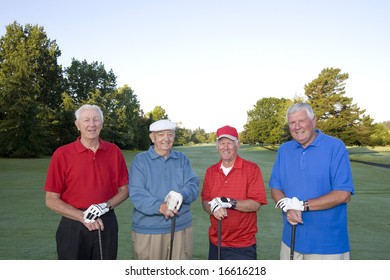 Four elderly men are standing together on a golf course. They are holding their clubs and smiling at the camera.  Horizontally framed shot.