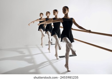 Four elegant girls, ballet dancers standing at barre and warming up, practicing against grey studio background. Focus on discipline. Concept of ballet, art, dance studio, classical style, youth - Powered by Shutterstock