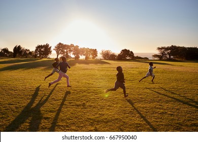 Four Elementary School Children Running In An Open Field