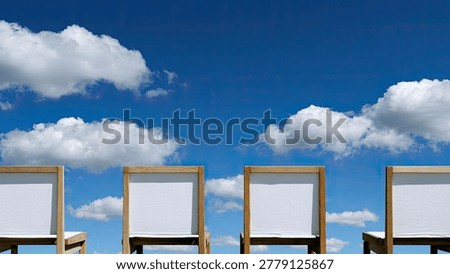 Four empty beach chairs are set up facing a bright blue sky with fluffy white clouds, suggesting a vacation or relaxation setting.