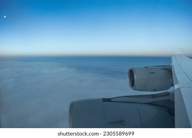 Four engine jet airplane in the dusk with moon visible over clouds