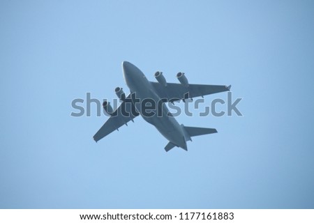 Four engine military cargo plane flying in the air. Dark grey plane silhouette with four jet engines, blue sky on the background.