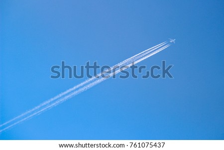 Four engined airplane flying through blue sky with long vapor trails