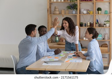 Four enthusiastic multiethnic staff members gather in office board room leaders of team giving high five gesture express unity share success, accomplish group meeting feel optimistic. Teamwork concept